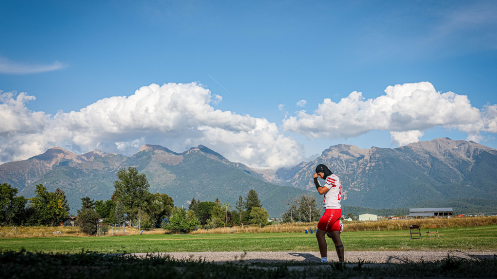 A football player with his fist to his head standing in front of mountains