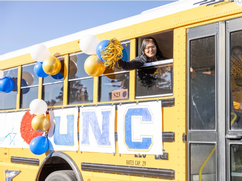 UNC Bear celebrating homecoming with on a UNC-decorated school bus, 2025