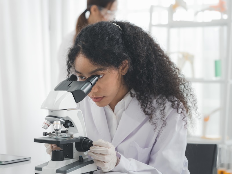 A female scientist is using a microscope to look and doing some experiments or research in the science room