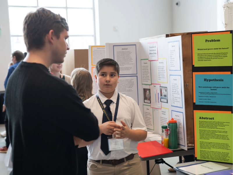 Photo of young science fair participant explaining his project to judge