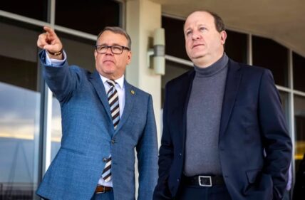 UNC President Andy Feinstein points to the COM building with Governor Jared Polis.