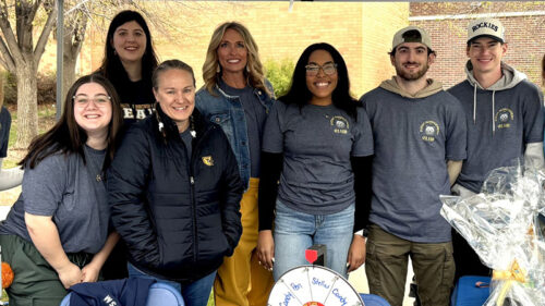 A group of people smiling at a booth with gift baskets, standing outdoors under a tent.