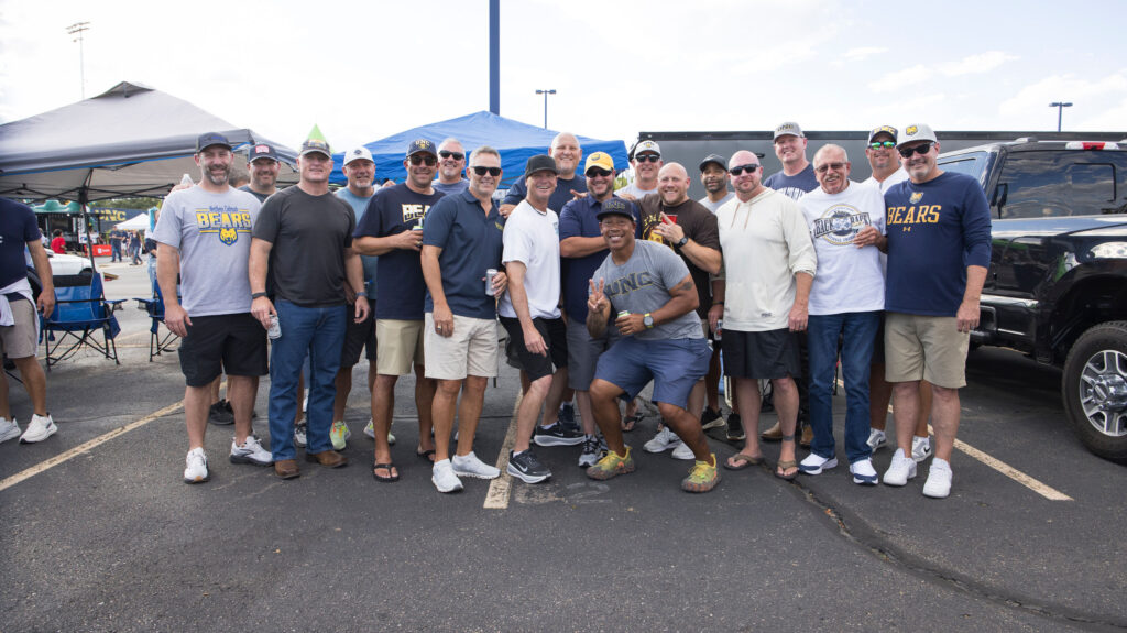 A large group of men standing together outside smiling at the camera