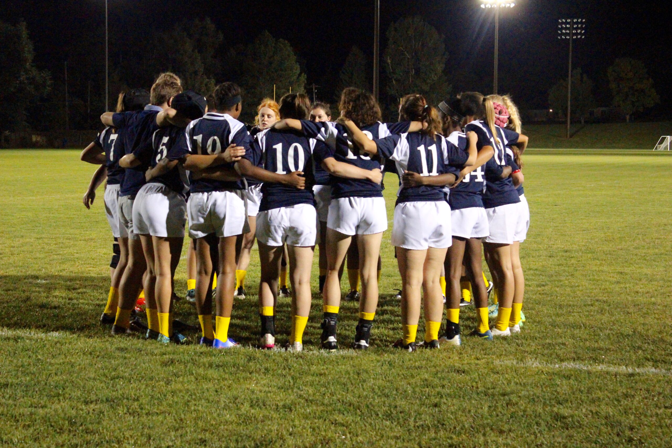 Photo of the Women's Rugby Club huddled together on the field