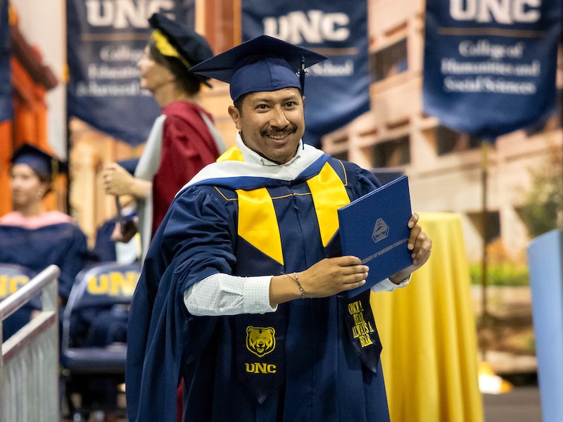 Male Hispanic student in graduation gown with degree