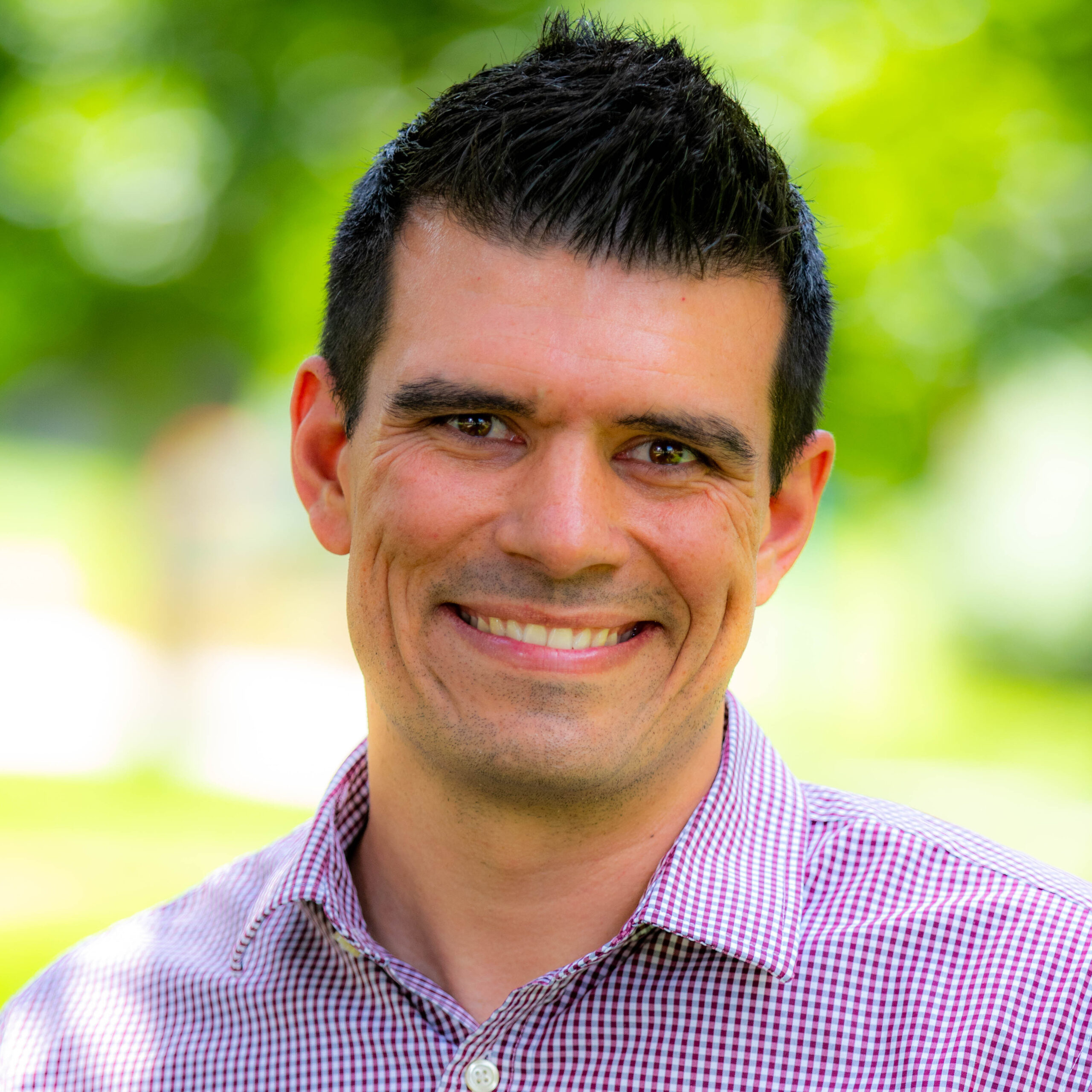 A man with dark hair, smiling with a green background