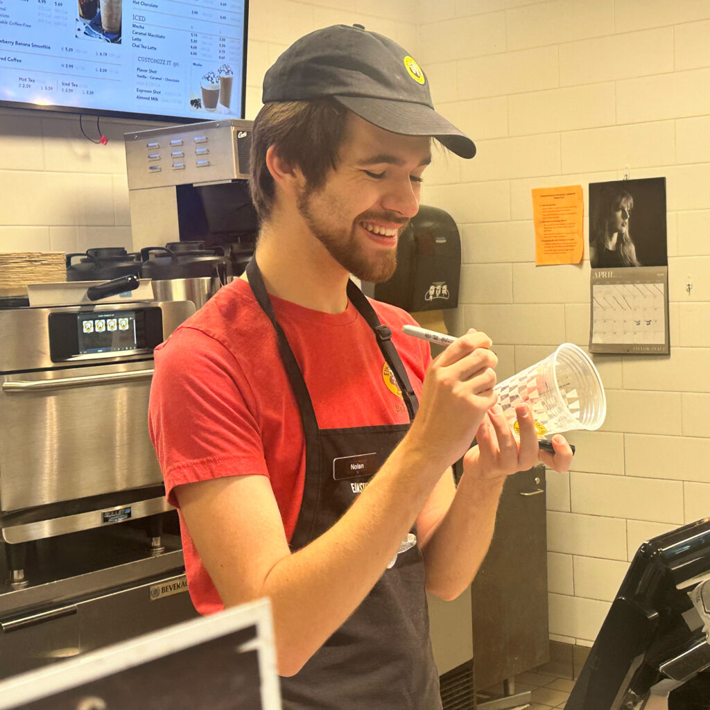 Nolan Bond smiling and writing on an Einstein's Bagel cup