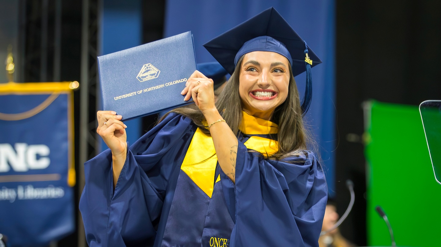 Female graduate holding up her diploma on graduate day