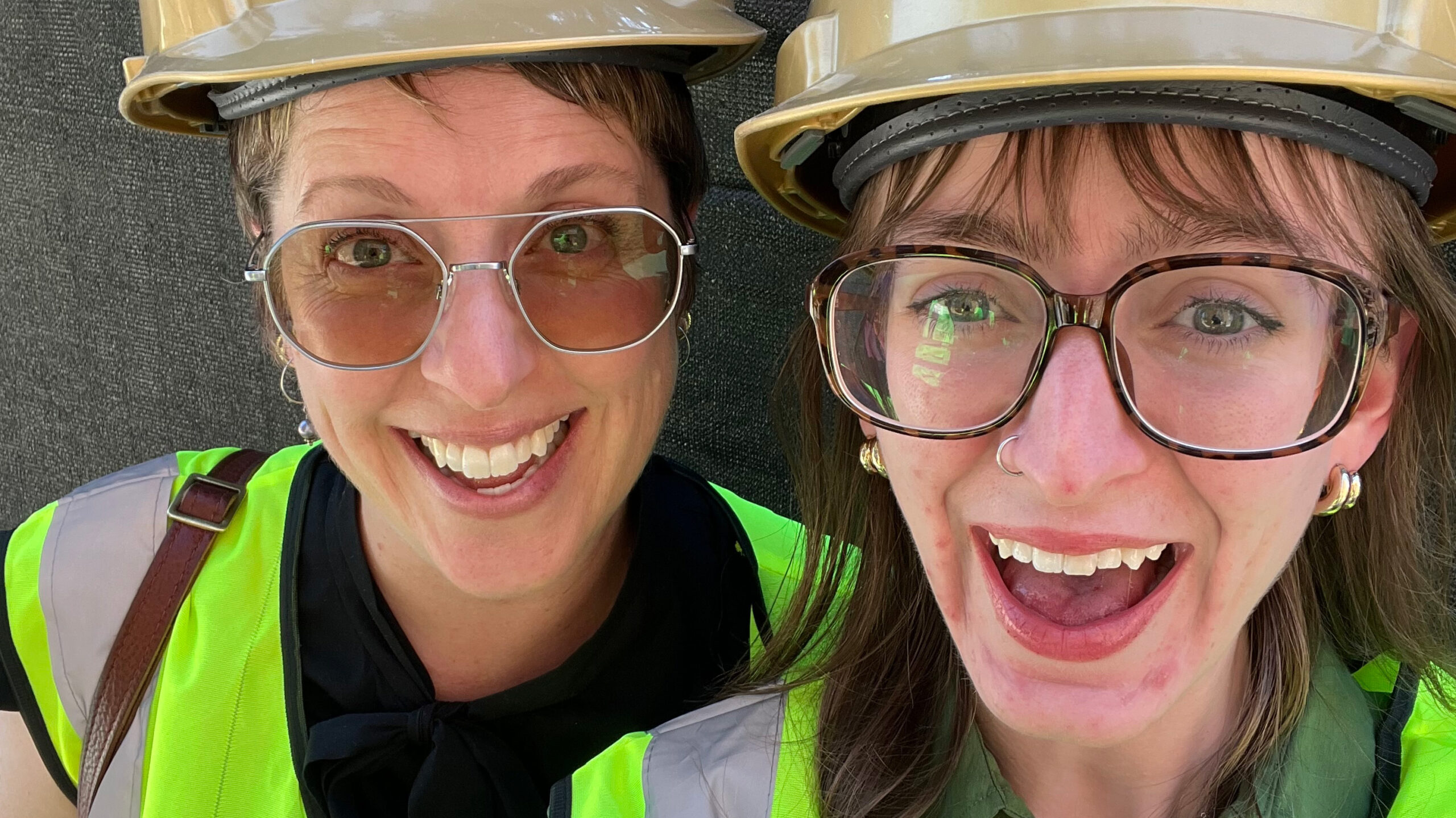 Two students wearing glasses, smiling and wearing green vests