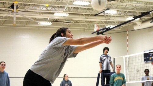 A student playing Intramural volleyball about to hit the ball with her teammates and official watching.