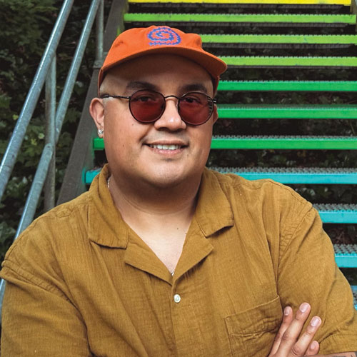 Adam Lucero wearing an orange hat and sunglasses and smiling at the camera