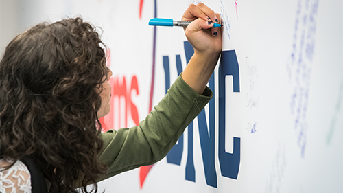 Aims2UNC student signing a banner.