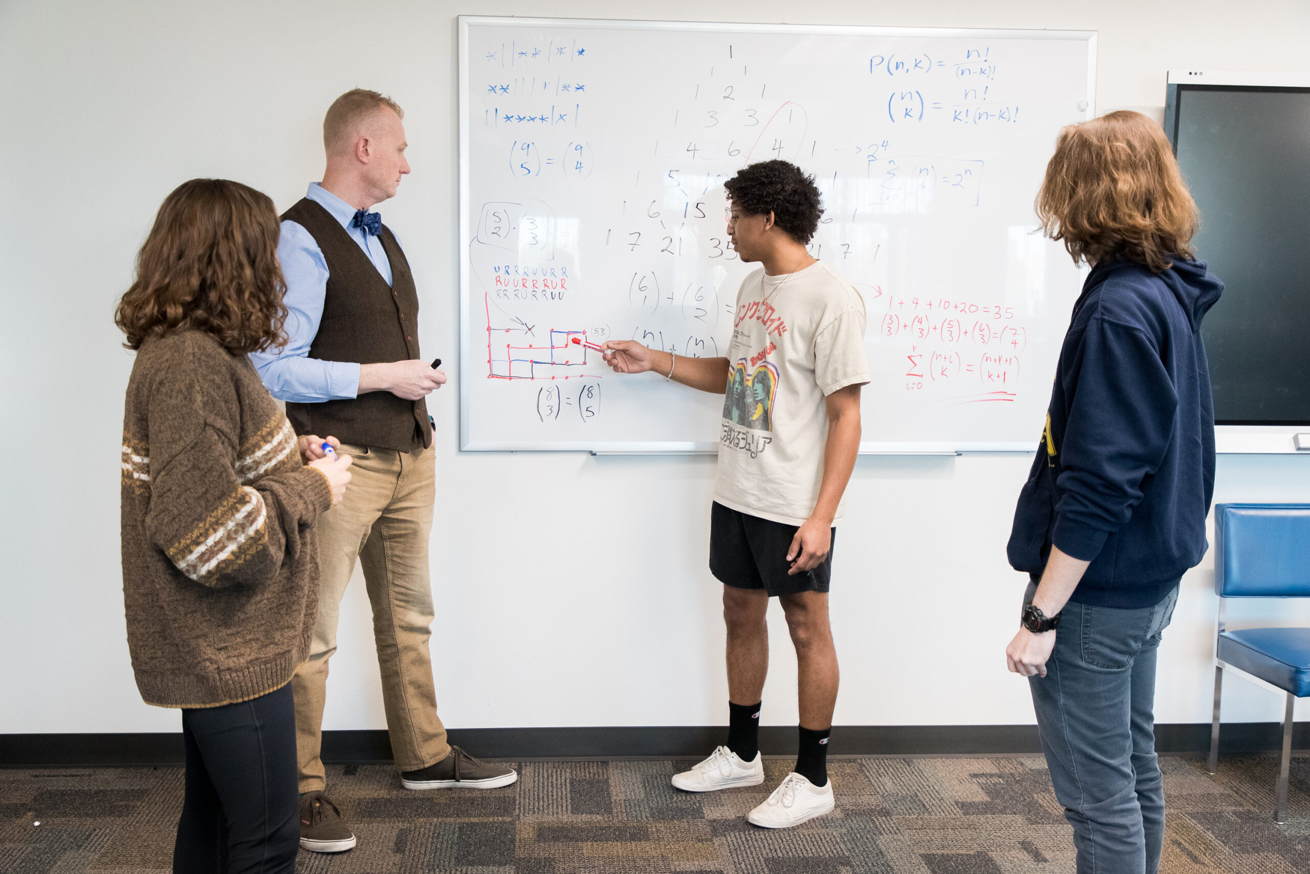 Students solving a equation with professor assistance in front of a white board