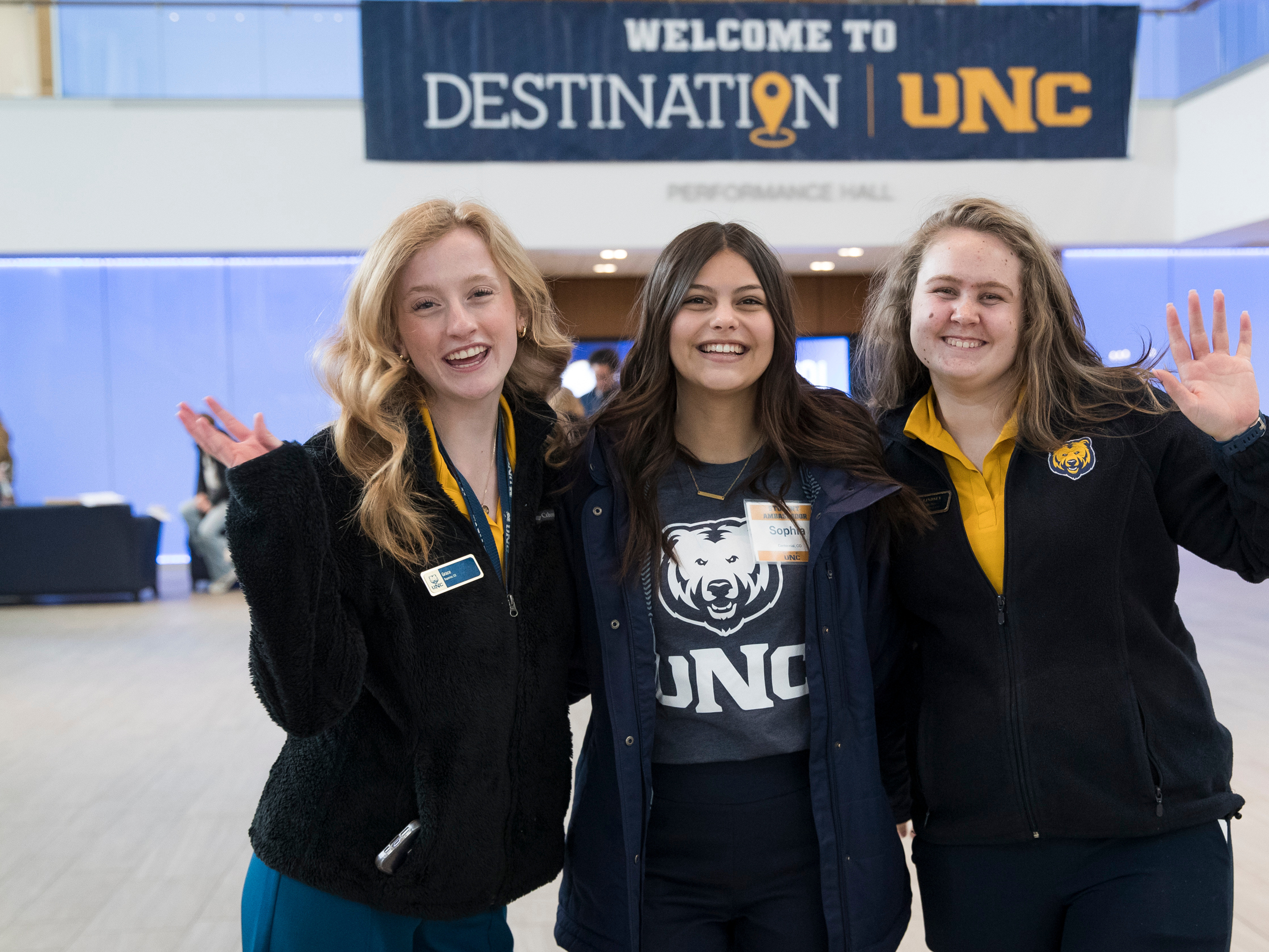 Three UNC Student Ambassadors waving at the camera with a 