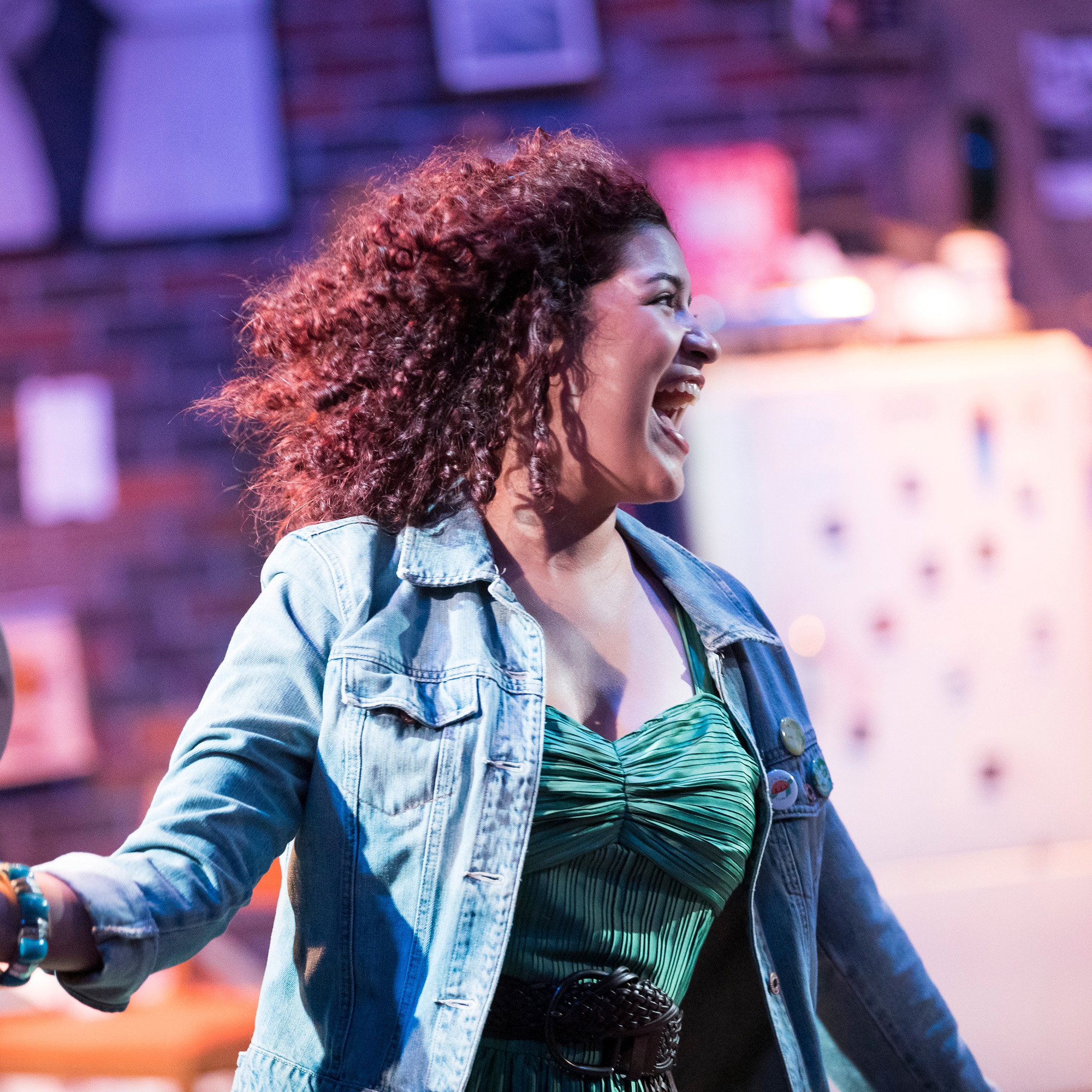 Recent UNC graduate Andrea Camacho with their head turned and smiling during their performance as Susan in Tick Tick Boom.