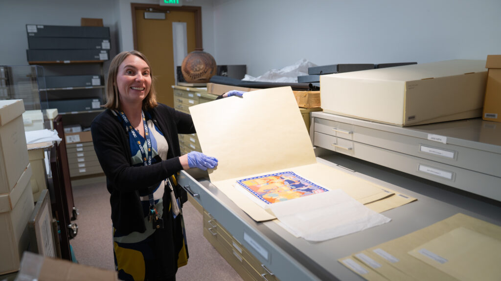 A librarian holding open a folder to display an image from the University Archives. The folder is in a flat file drawer which is open.