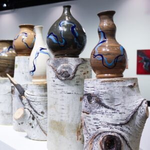 Ceramic artwork sitting on tree stump pedestals on view at the 2026 MA Thesis Exhibition at the UNC Ruyle Gallery.