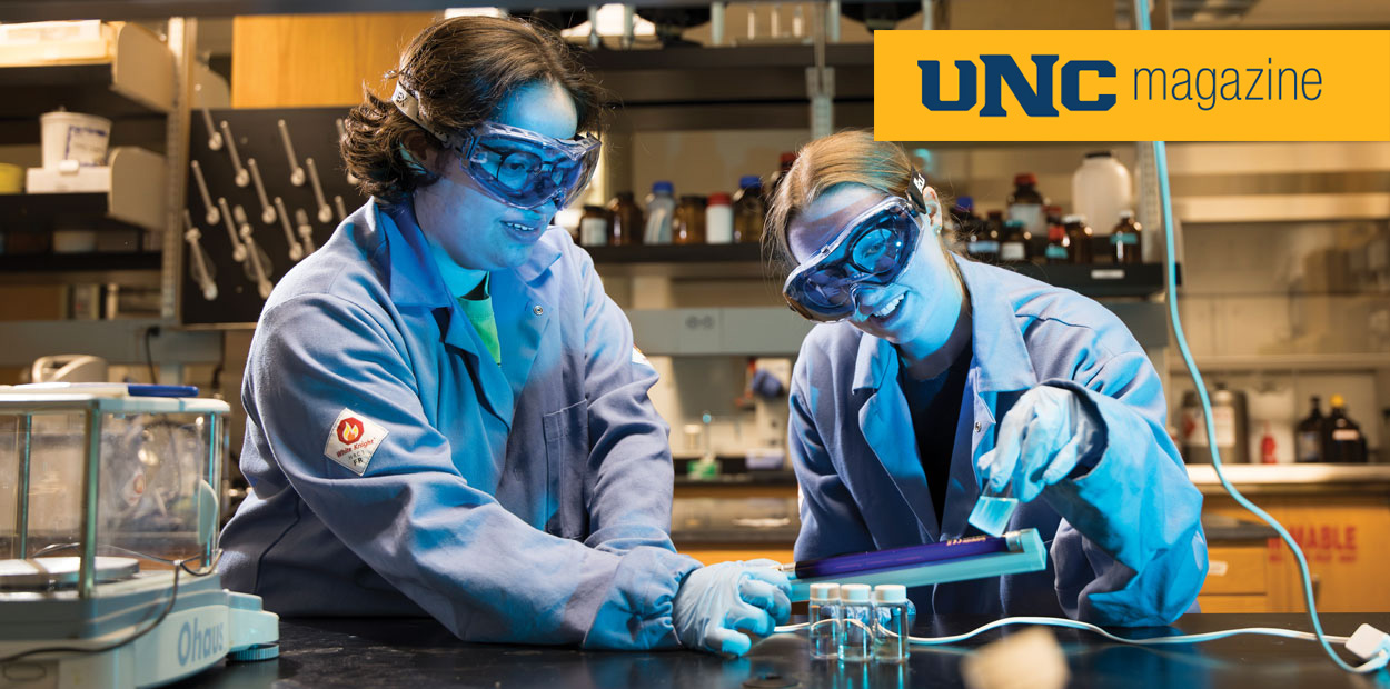 Two students wearing safety glasses and lab jackets doing some research