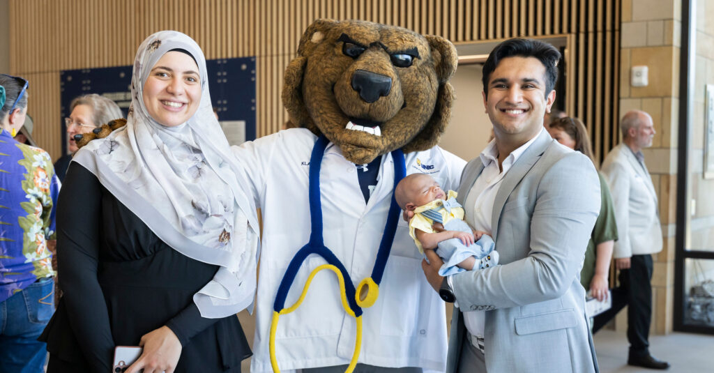 A med student holding his baby smiling next to Klawz and his wife