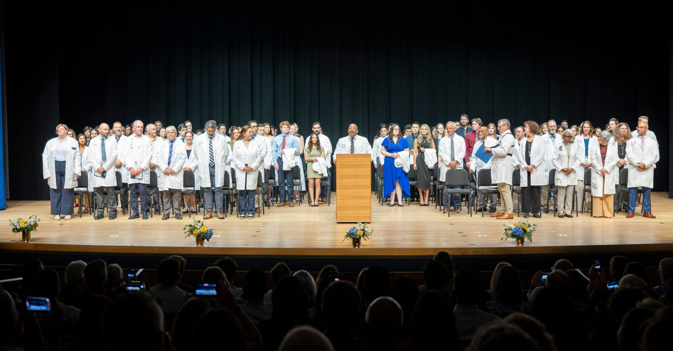 All of the students standing on the stage of the white coat ceremony