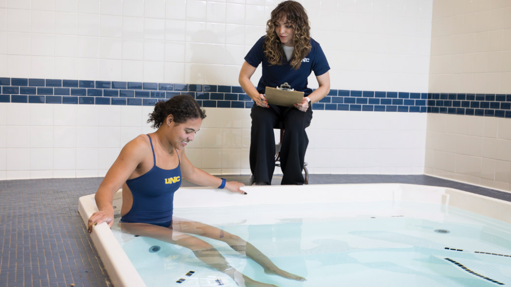 A student sitting in a cold plunge pool as a CHIPC staff member monitors from the side.