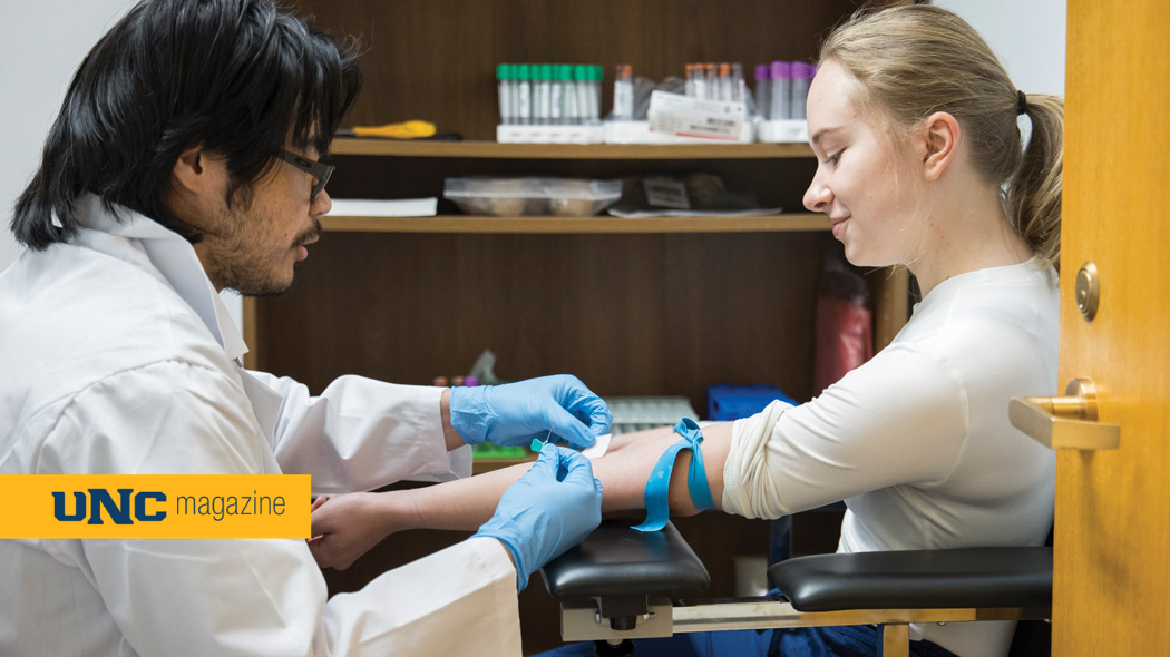 A young medical student in a lab coat drawing blood from a patient.