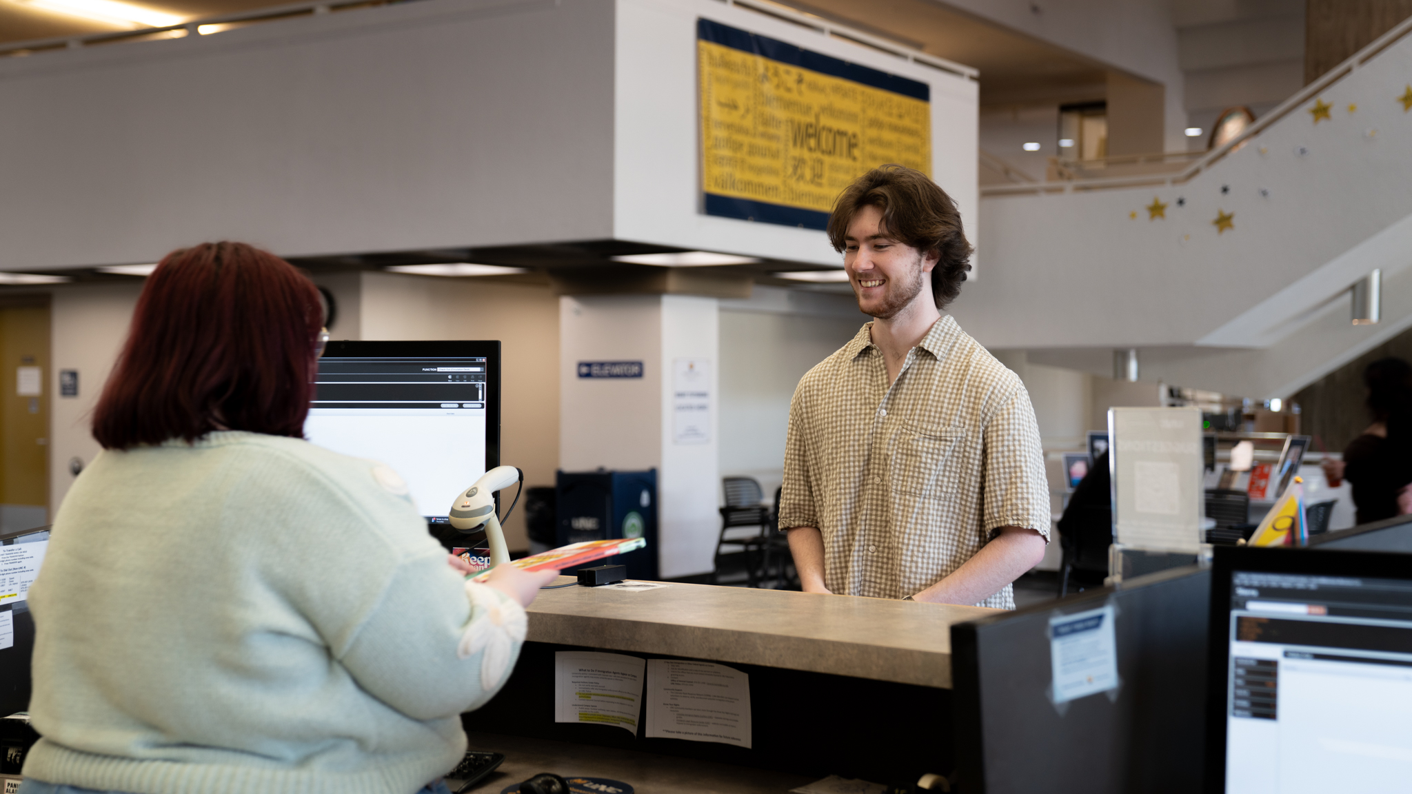 A library staff member hands an item to a patron at the Michener Library circulation desk