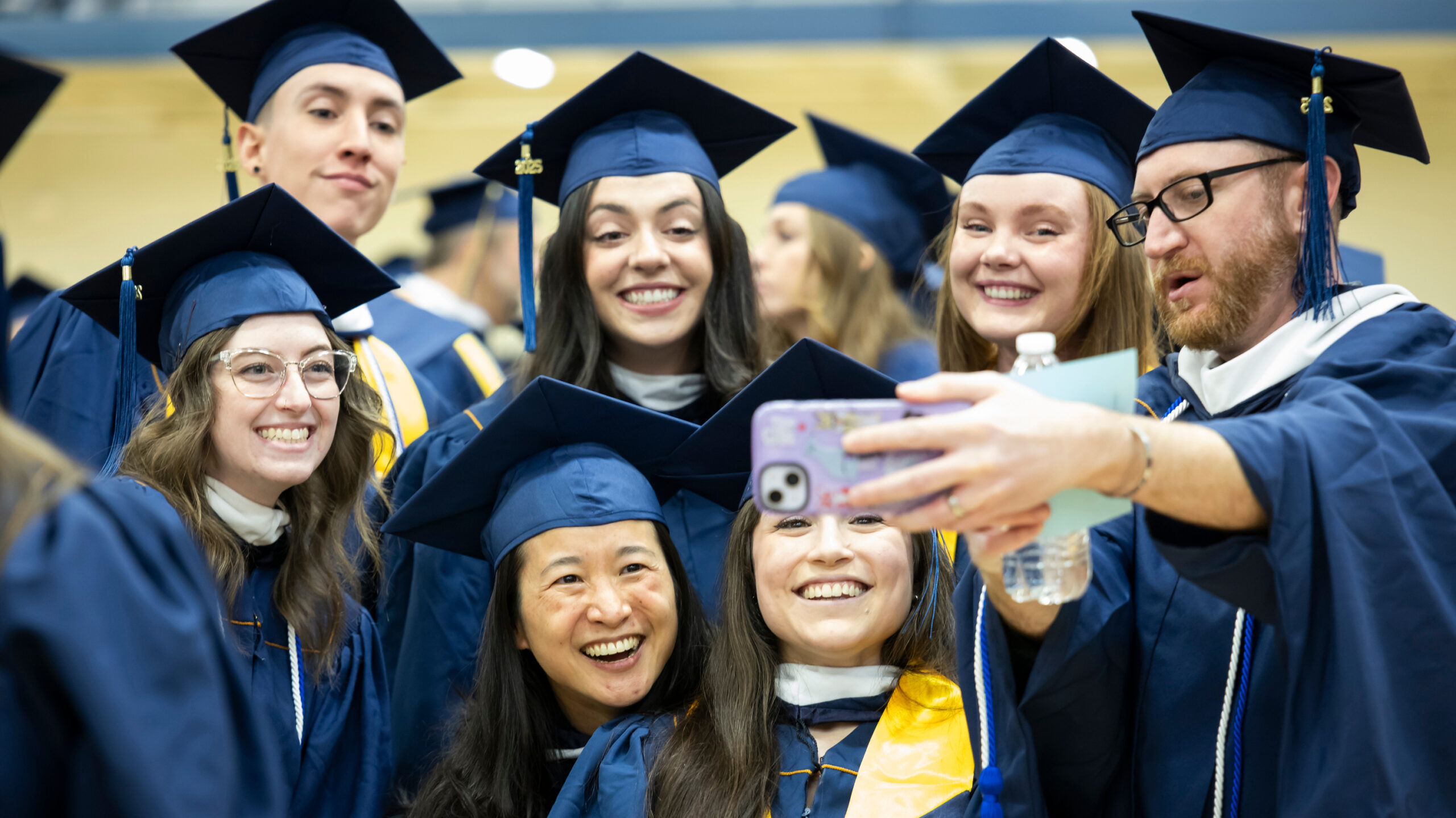 Group of UNC graduates in cap and gown smiling and taking a selfie together