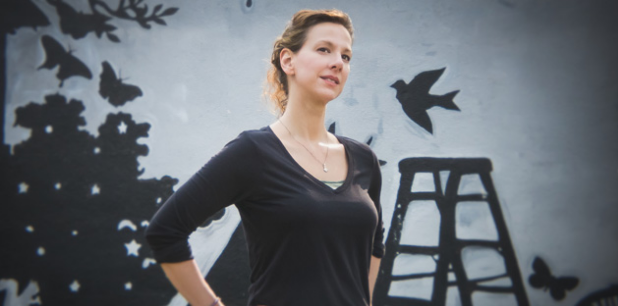 A woman standing in front of a mural of a bird, butterflies and other nature.