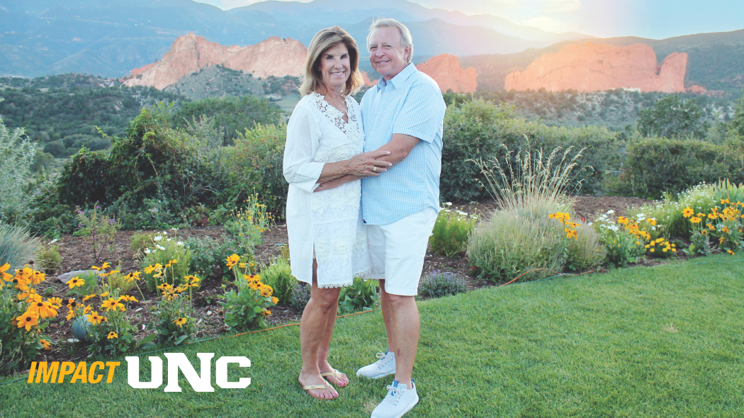 UNC alums Rob and Michele Edmisson standing on a lawn in front of a scenic backdrop of hills and rocks.
