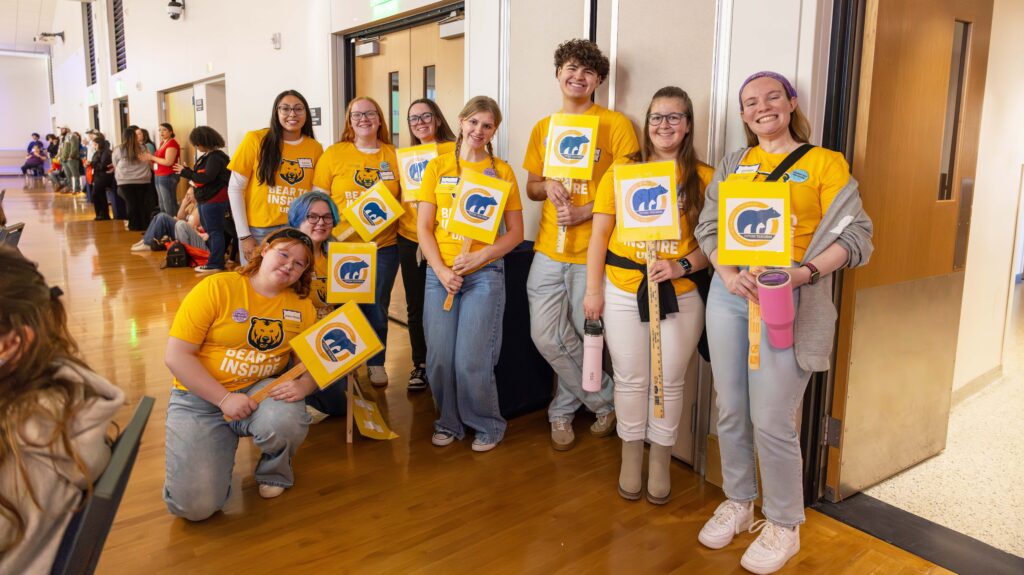 A group of UNC students holding yellow signs and wearing yellow shirts smiling at the camera