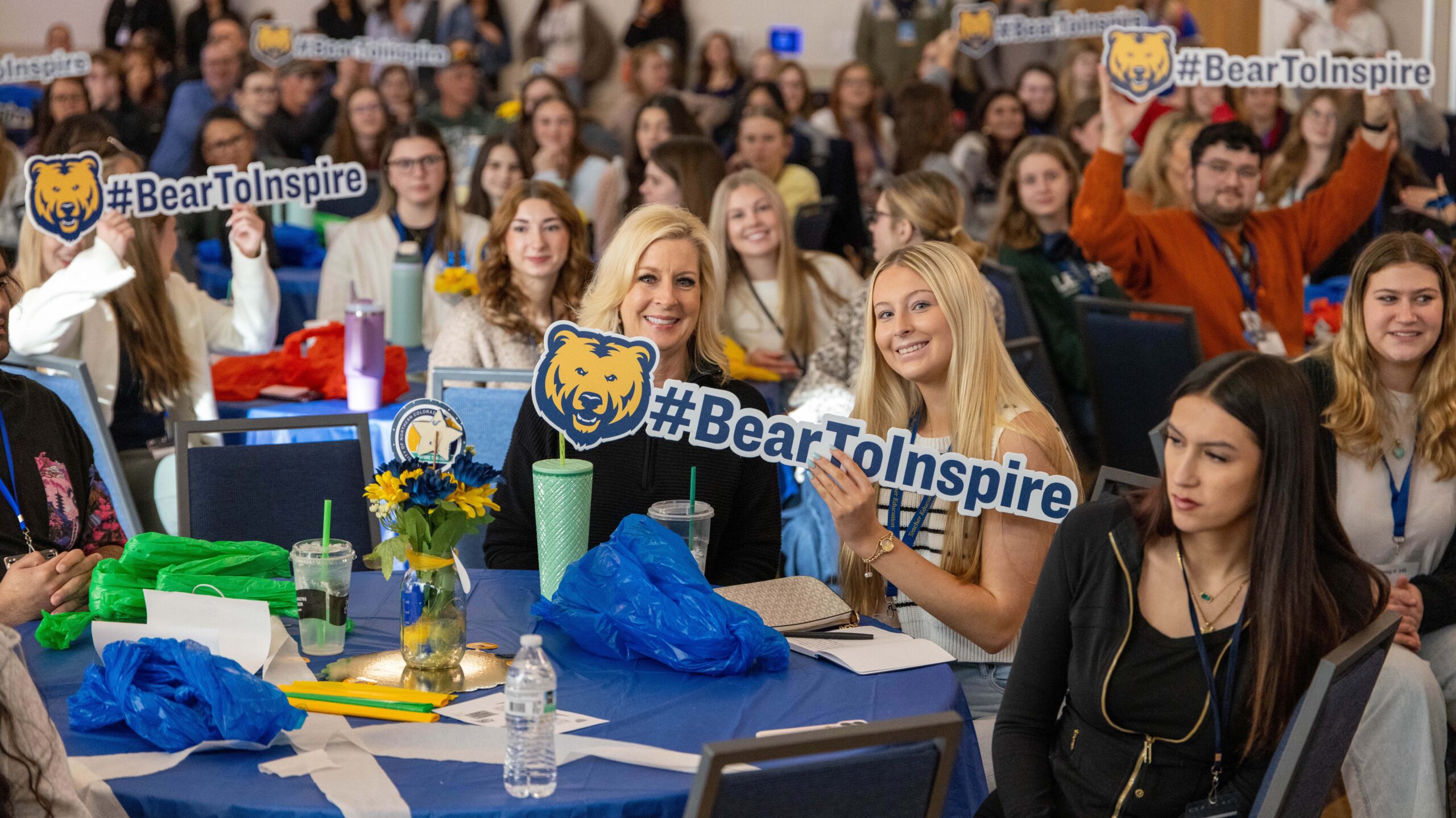 A group of people sitting in chairs holding up a sign that says # Bear To Inspire