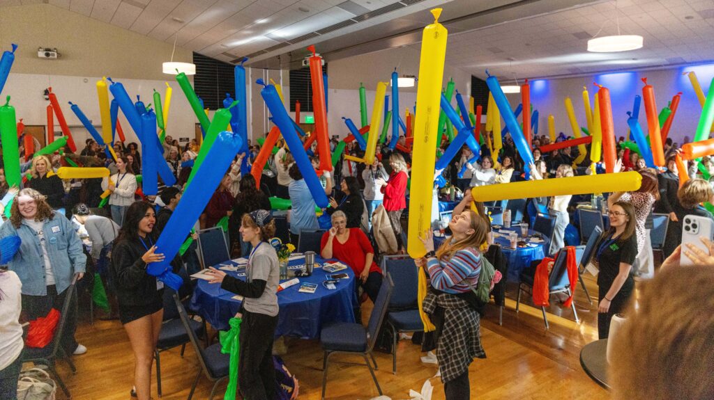 A group of people standing and holding up long colorful balloons in the air