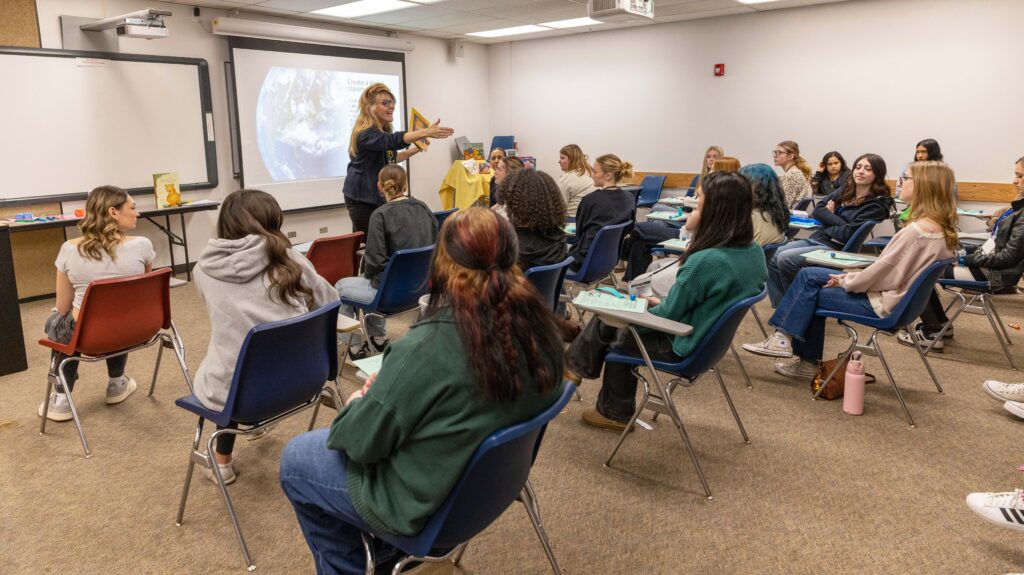 A teacher in the classroom talking to room full of students in chairs