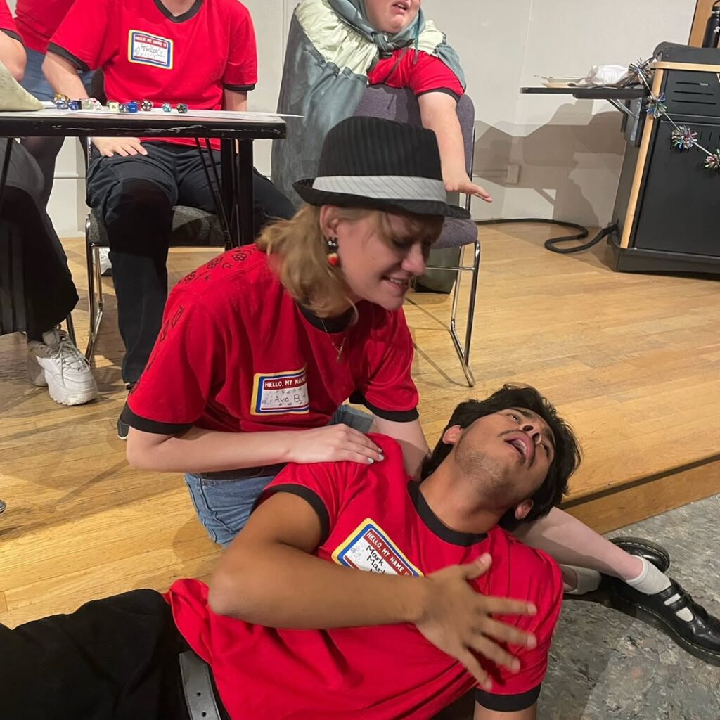 A student putting her hand on another student who looks like they have fake fallen down in distress