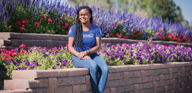 Joelle Jenkins sitting on a brick ledge with flowers surrounding behind her