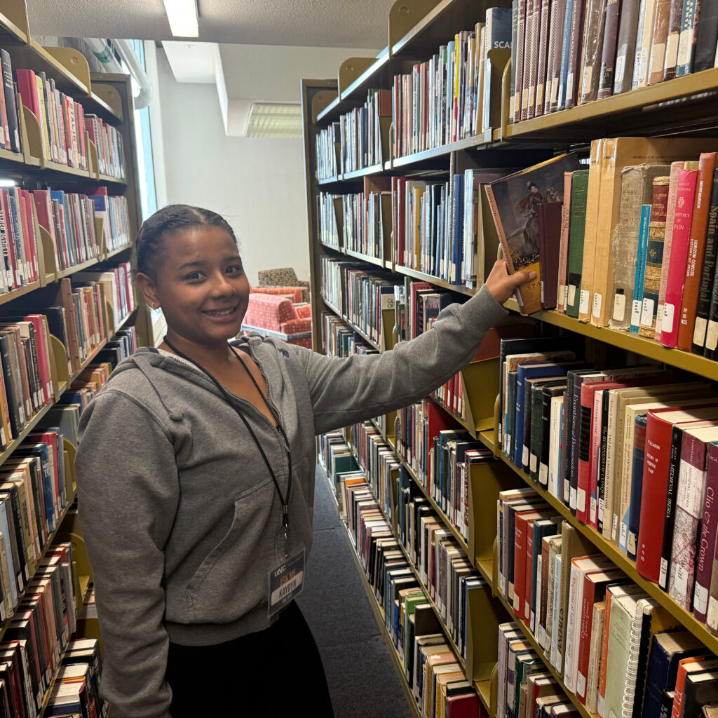 Kaydyn Richey smiling at the camera and putting a library book back on the shelf