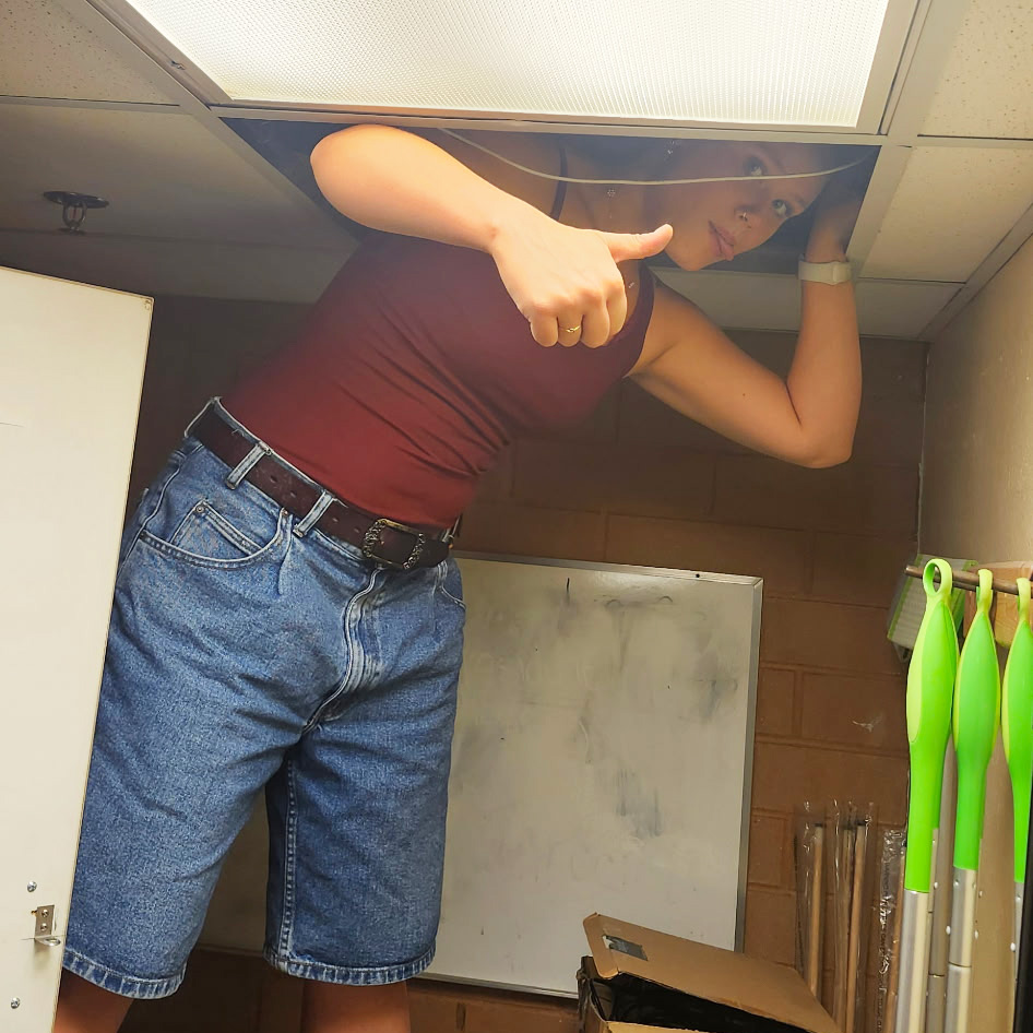 Keira Bowman with her head in the ceiling working on electrical wires.