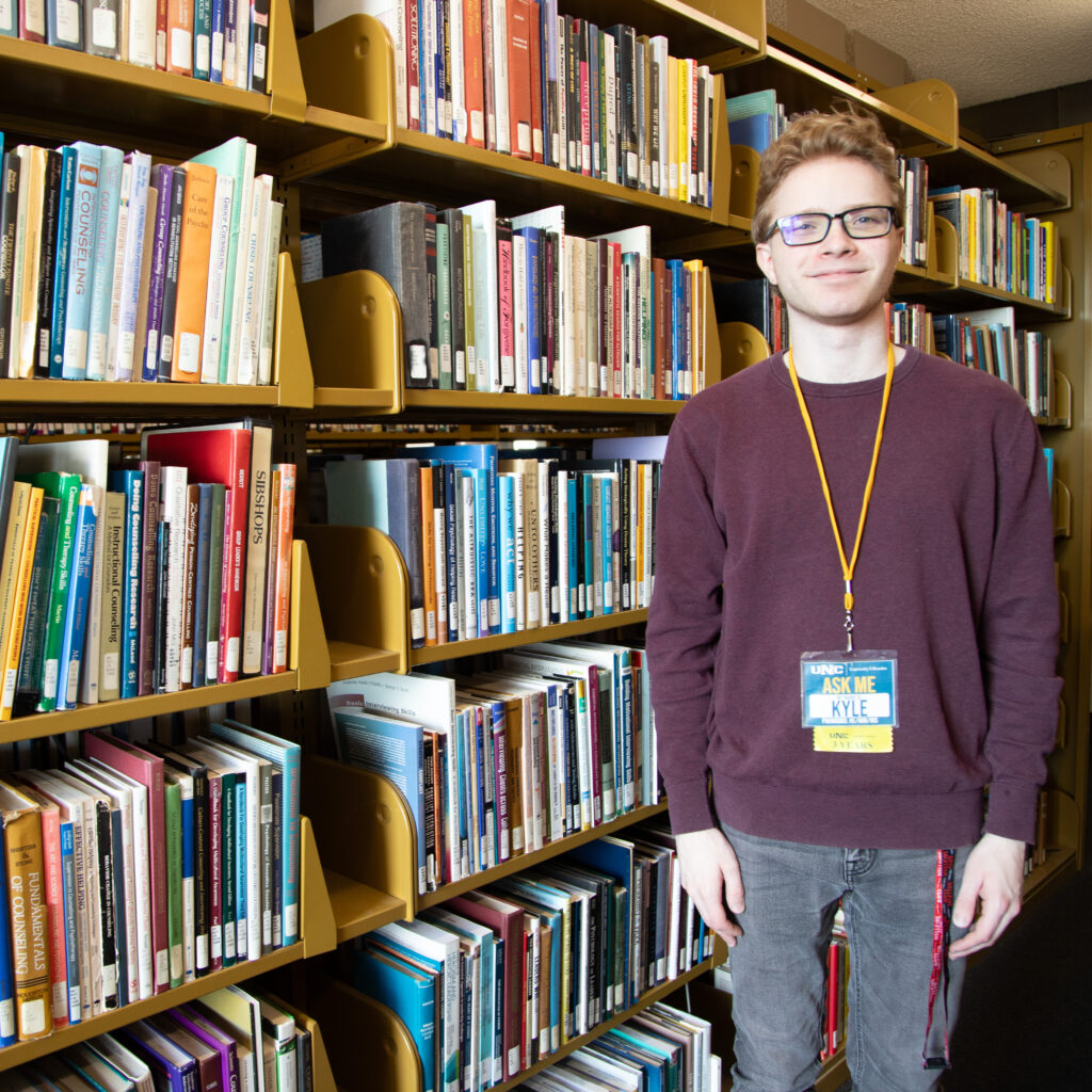 Kyle Yoder smiling at the camera standing in front of shelves of books