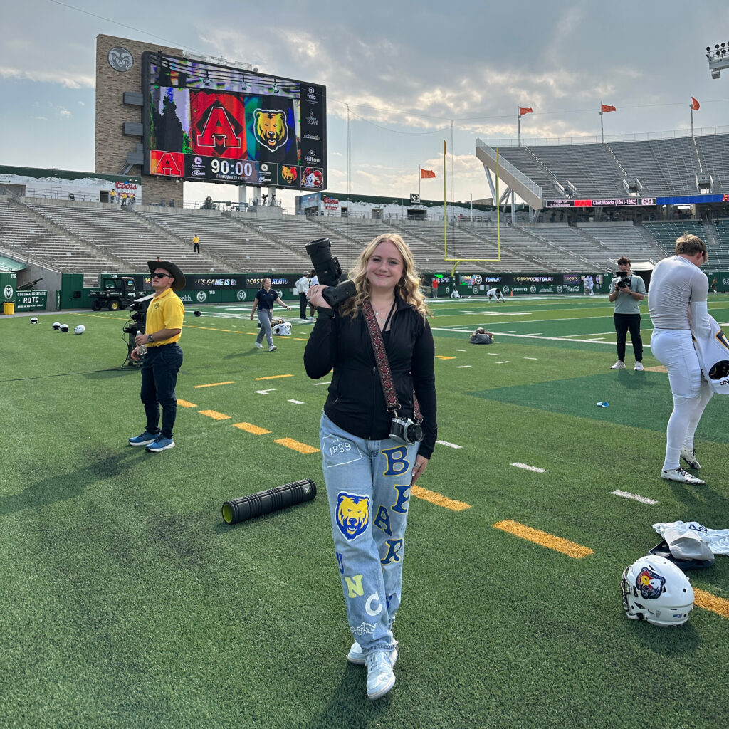 Lexie Martin standing on a football field holding up a camera