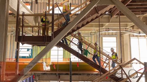Inside the COM building under construction. Construction workers walking up the stairs.