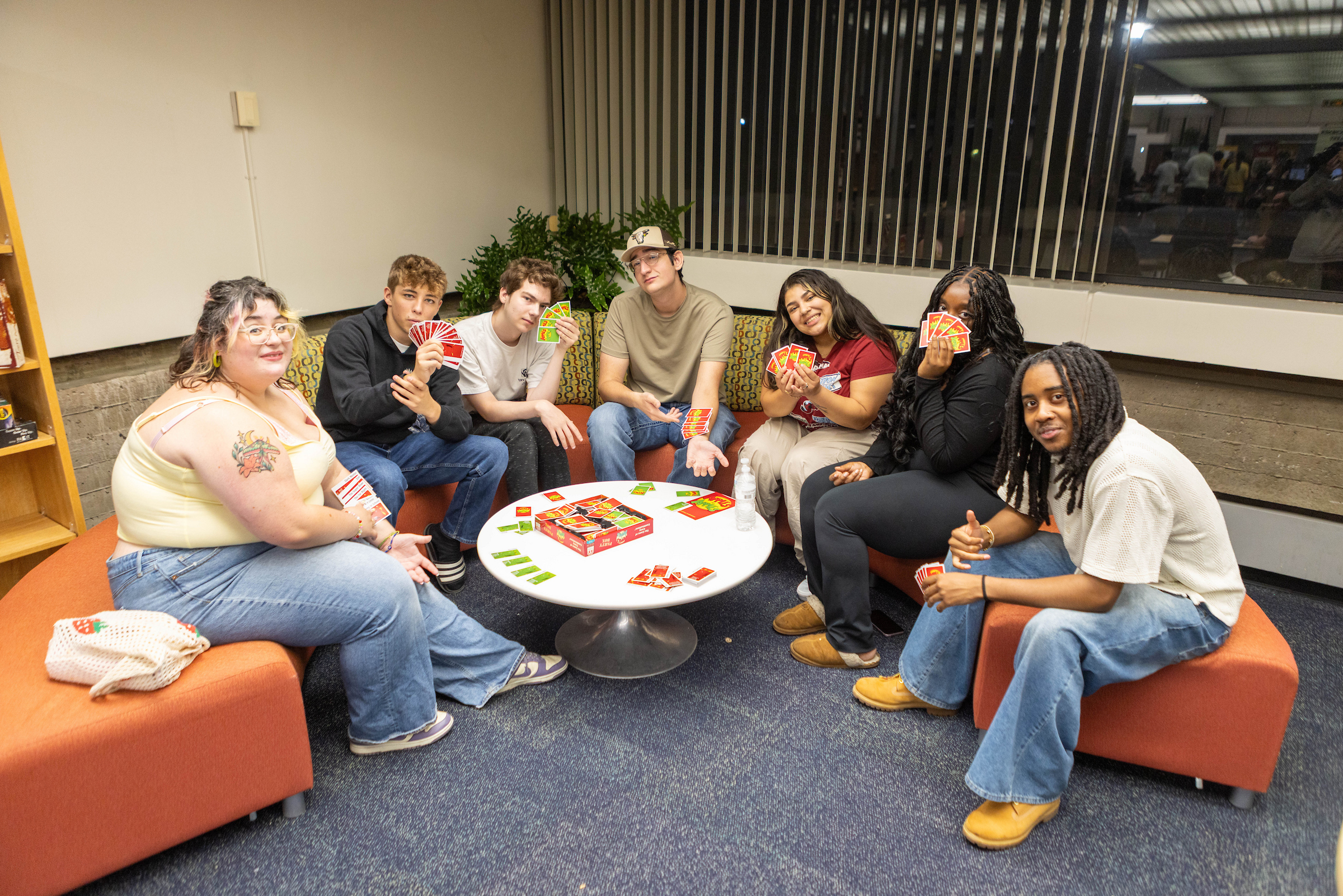 Students sit around a lounge table, holding cards during game night at UNC.