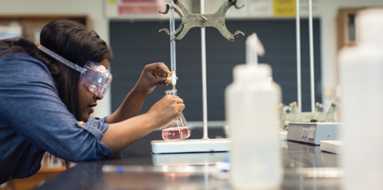 A student wearing safety goggles performing a chemistry experiment.