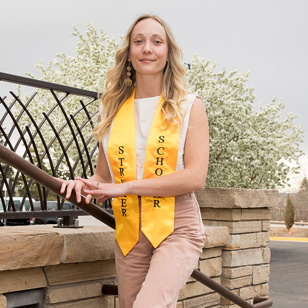 Madeline Dannewitz, a recent UNC graduate, leaning on a handrail, wearing her Stryker Scholar stole.
