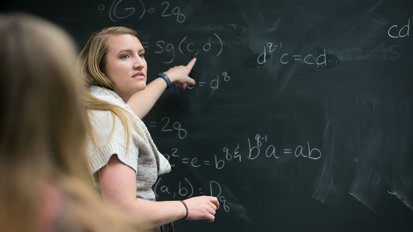 Student pointing to an equation on a blackboard.