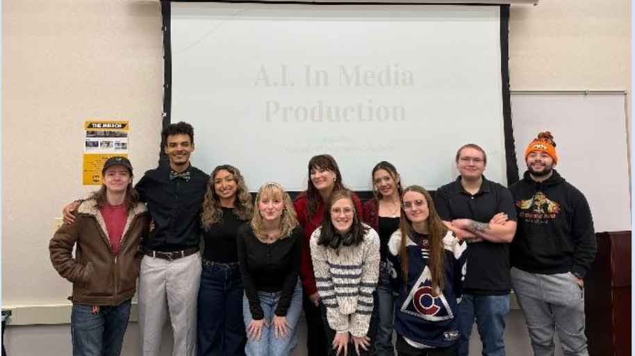 A group of students standing in front of a projection screen smiling