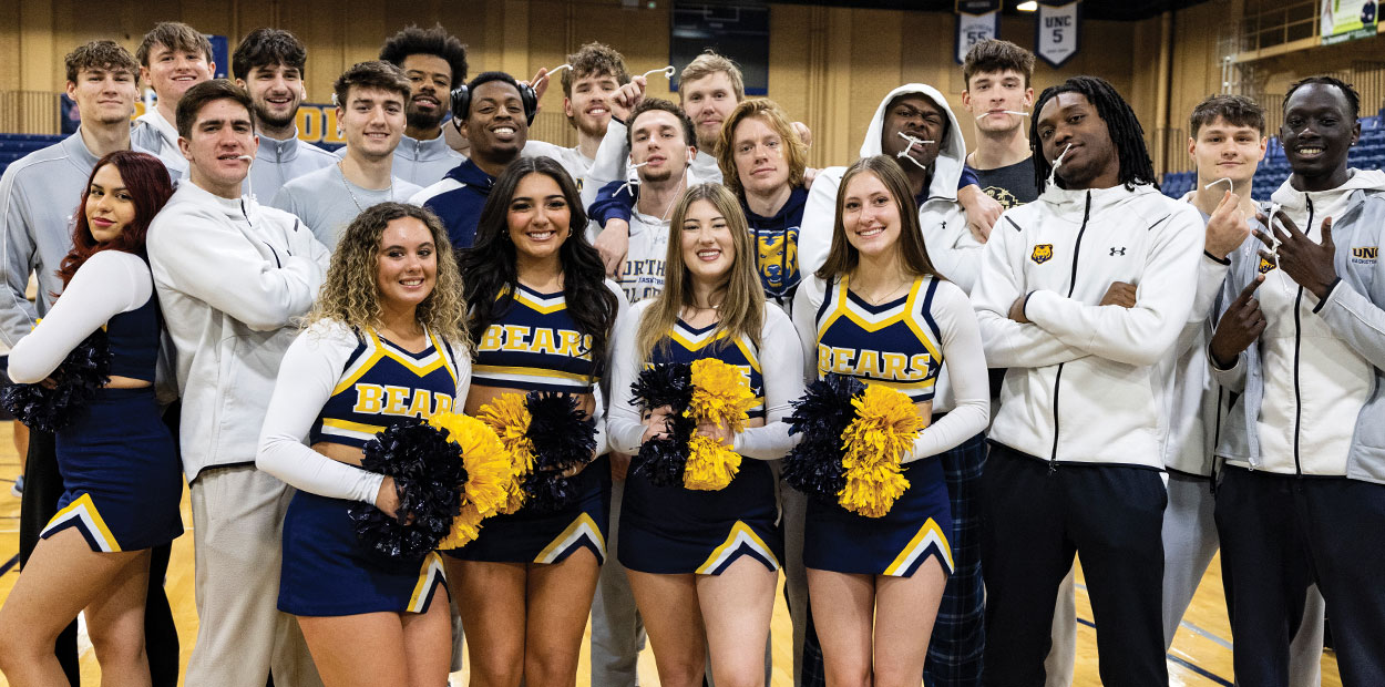 The men's basketball team posing with some UNC cheerleaders, all standing and smiling