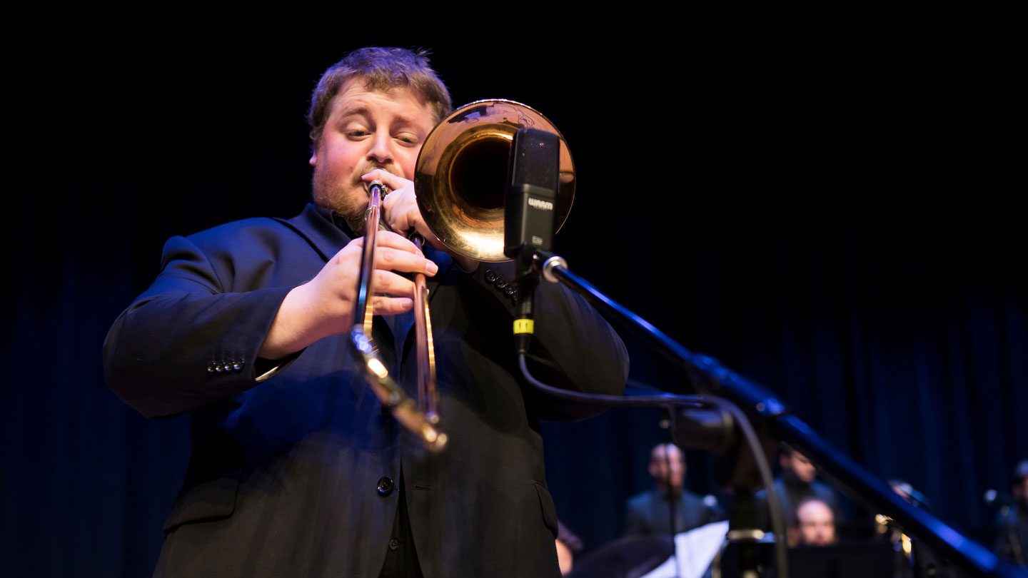 Performer playing a trombone into a microphone.