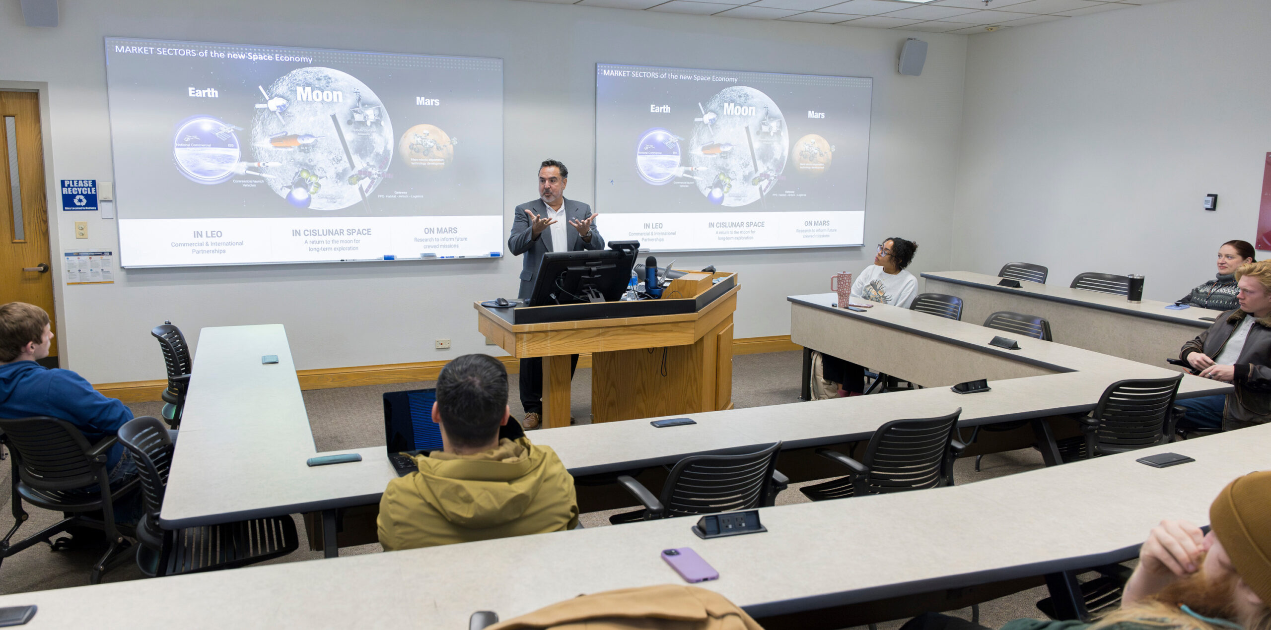 Walt Ugalde standing at a guest in a lecture hall with space images behind him
