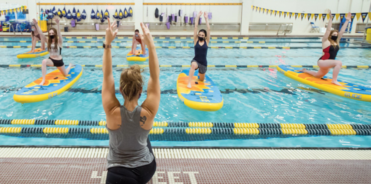 A group yoga class where participants balance on surf boards in a pool.